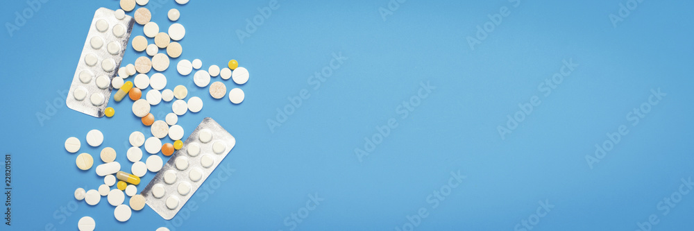 Pills of different colors on a blue background. Concept of the pharmaceutical industry, medicine, treatment and recovery after illness. Banner. Flat lay, top view