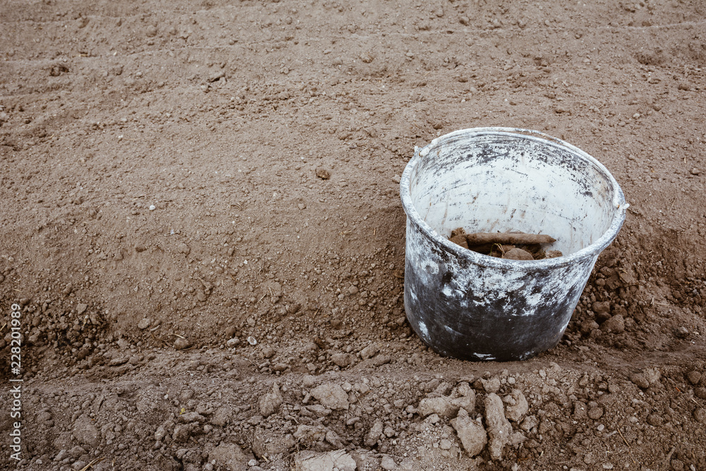 Old bucket covered in paint in the garden between rows with stones and weeds in it after cleaning ground. Work concept, copy space. Film effect. Old bucket covered in paint in the garden between rows with stones and weeds in it after cleaning ground. Work concept, copy space. Film effect.