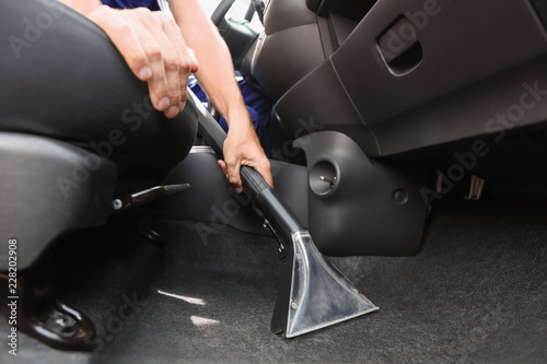 Man cleaning automobile salon with vacuum cleaner, closeup. Car wash service photo