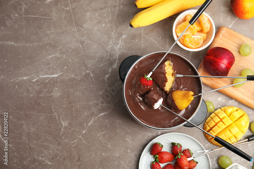 Flat lay composition with chocolate fondue in pot, fruits and space for text on gray background