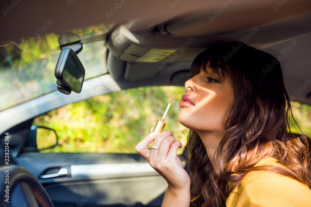 Portrait of beautiful woman looking in rear view mirror and putting make up in car Portrait of beautiful woman looking in rear view mirror and putting make up in car