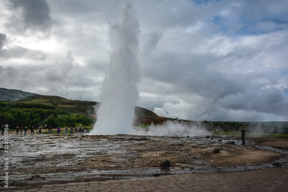 Eruption of Strokkur geyser in Iceland in summer with many tourists in the background