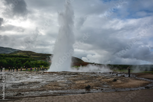 Eruption of Strokkur geyser in Iceland in summer with many tourists in the background