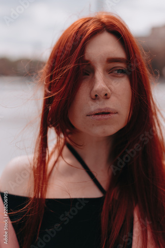 Beautiful and stylish girl with red hair walks in the city and her hair is in the wind