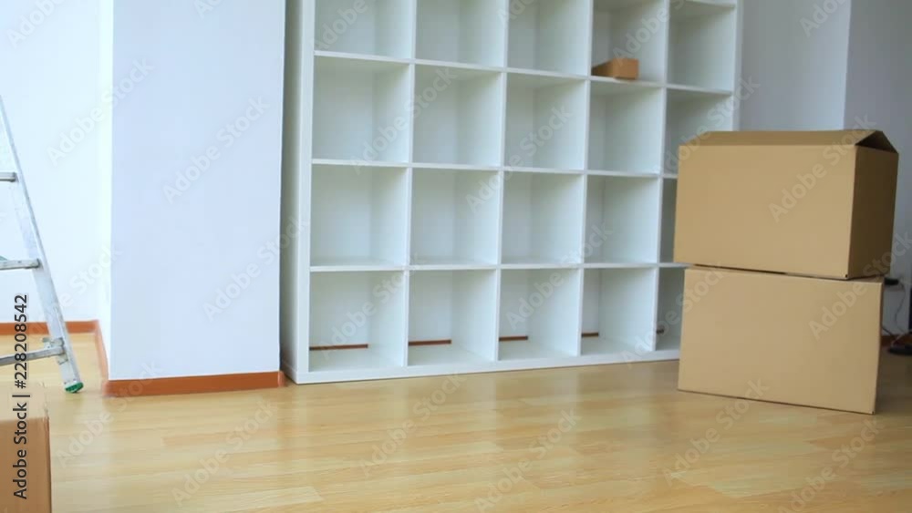 Real Eatate. Happy Young Couple Moving House Together With The Pretty Young Woman Sitting Inside a Brown Cardboard Box With Her Husband Crouching Alongside Smiling Real Eatate. Happy Young Couple Moving House Together With The Pretty Young Woman Sitting Inside a Brown Cardboard Box With Her Husband Crouching Alongside Smiling