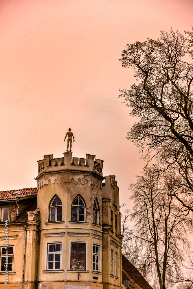 Statue of a man on top of the old building in Kuldiga, Latvia at dusk. One window is missing. Artistic altered vanilla skies.