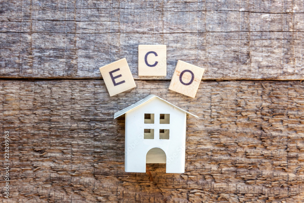 Miniature toy model house with inscription ECO letters word on wooden backdrop. Eco Village, abstract environmental background. Real estate mortgage property insurance sweet home ecology concept