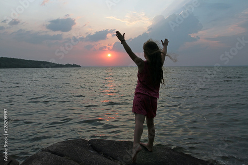 Silhouette of a young girl standing on the background of the sunset and the sea with outstretched arms photo