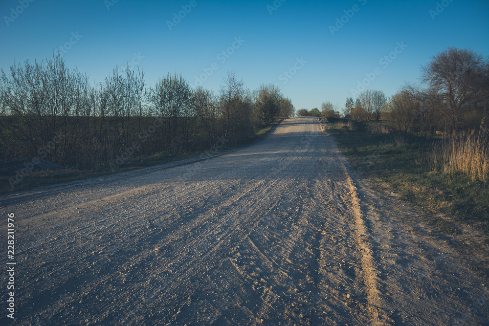 Empty gravel road in countryside in perspective with trees in surroundings.  Summer colors. Vintage style.