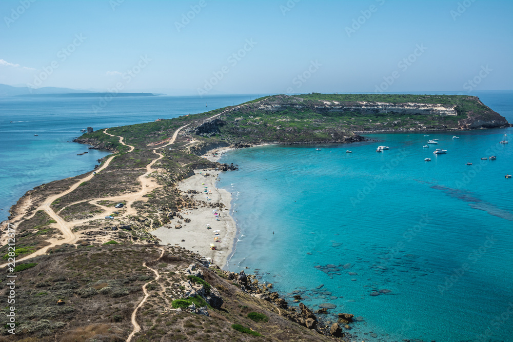 San Giovanni di Sinis coastline on a sunny day with yachts in the background in the turquoise sea. Sinis peninsula, Cabras, Oristano province, Sardinia, Italy.