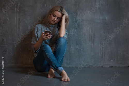 Helpline, psychological assistance. Suffering young woman sitting in a corner with a phone in her hand