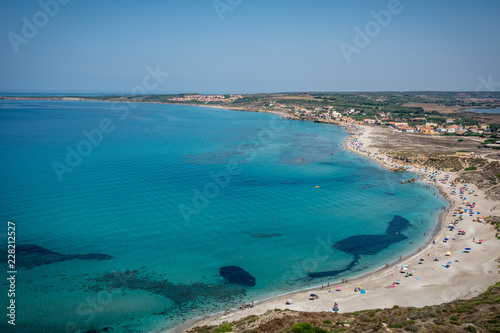 Beach view to colorful beach umbrellas and unrecognizable people in turquoise sea on a sunny day. San Giovanni di Sinis coastline, Cabras, Oristano province, Sardinia, Italy. 