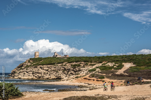 Capo Mannu Cliffs with blue sky, dramatic clouds and some unrecognizable cyclists. Shot in Capo Mannu beach, Sardinia, Italy
