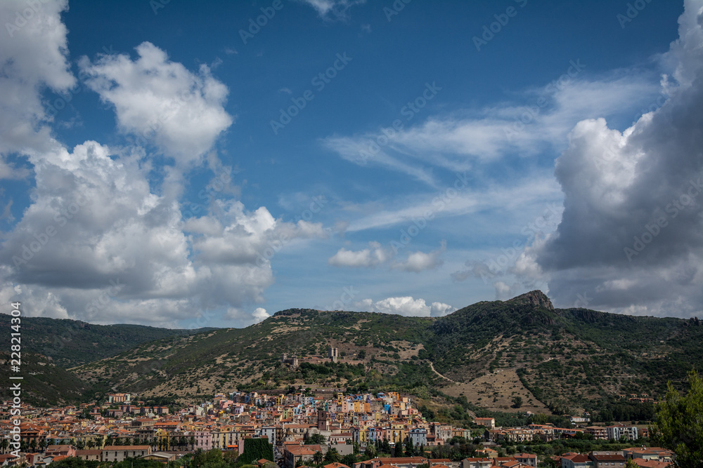 City view of Bosa, Sardinia, Italy from above. Colorful houses, mountains and cumulus clouds on a sunny day.
