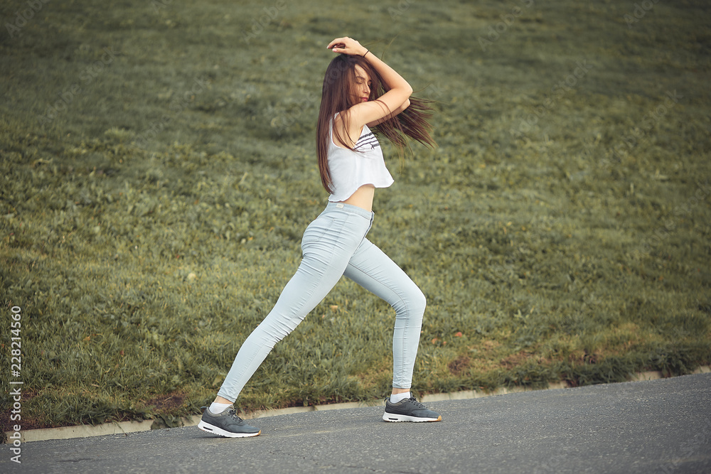 a young girl dancing on the street in the summer in the city against the green grass. a young girl dancing on the street in the summer in the city against the green grass.