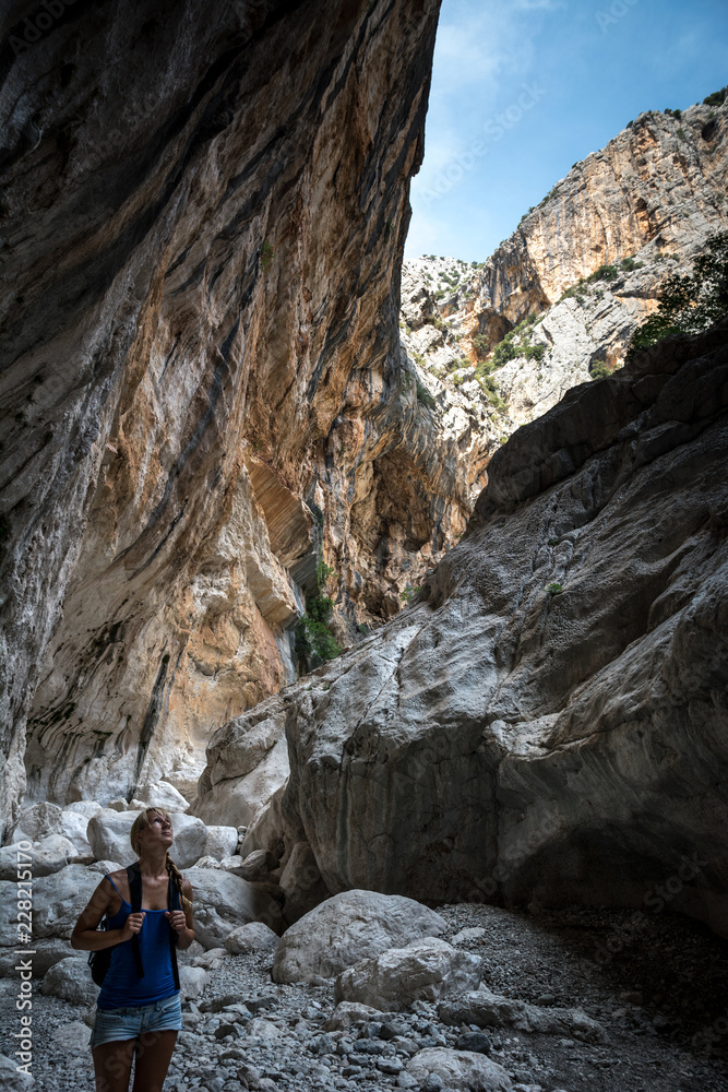 Young woman standing in canyon and looking up at the top of canyon.  Gola Su Gorropu canyon, Sardinia, Italy - important natural site in Sardinia. 