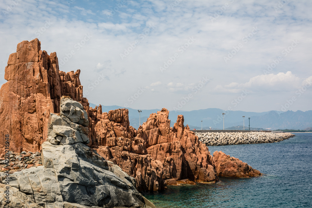 Red rocks of Arbatax city, Sardinia, Italy. Pier, beautiful blue sky with some clouds and sea on a sunny summer day. Nobody in the scene.