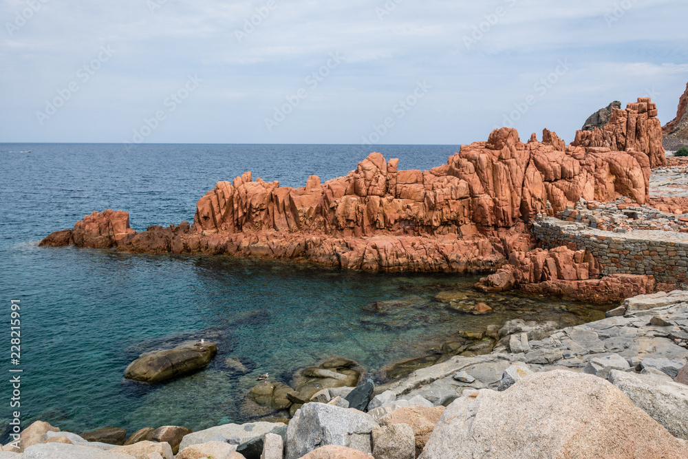 Red rocks of Arbatax city, Sardinia, Italy. Beautiful blue sky with some clouds and small beach on a sunny summer day. Nobody in the scene.