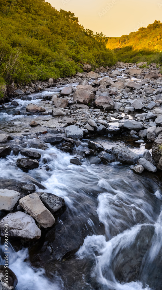 Typical view in Skaftafell national park to the river and stones, water in motion blur, Iceland in summer, sunset colors Typical view in Skaftafell national park to the river and stones, water in motion blur, Iceland in summer, sunset colors