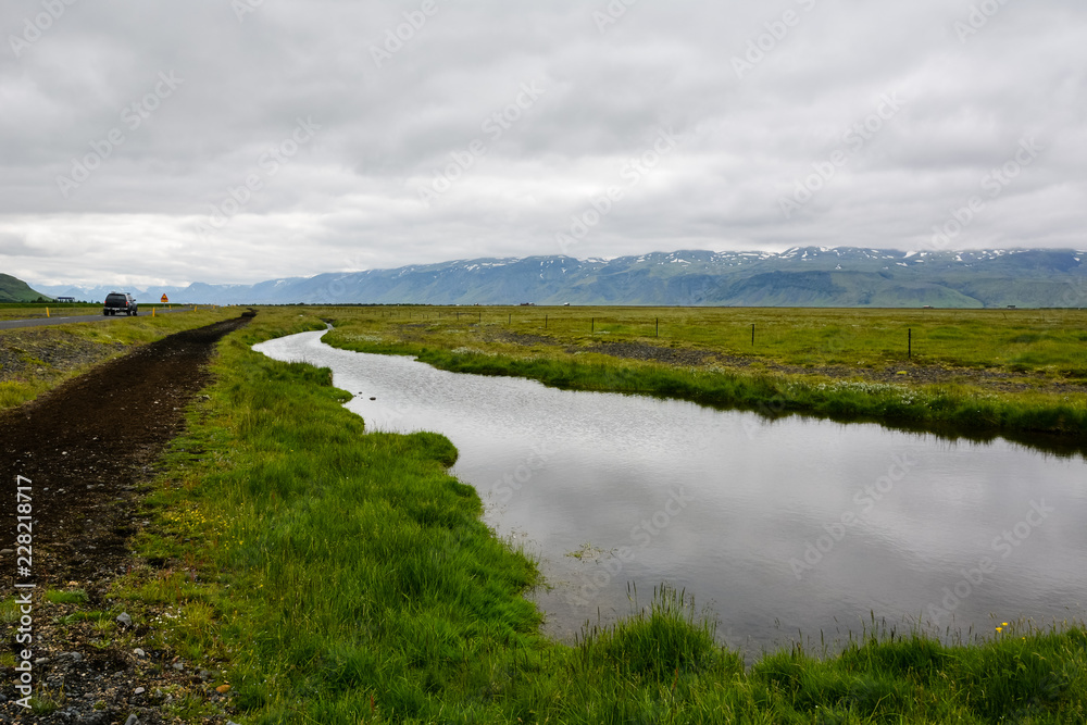 Empty road with view to, mountain with small river along the way on overcast day in Iceland. Car on sideway.