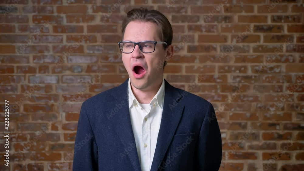 Yawning caucasian guy is standing next to camera on brick background and looking tired and relaxed indoor Yawning caucasian guy is standing next to camera on brick background and looking tired and relaxed indoor