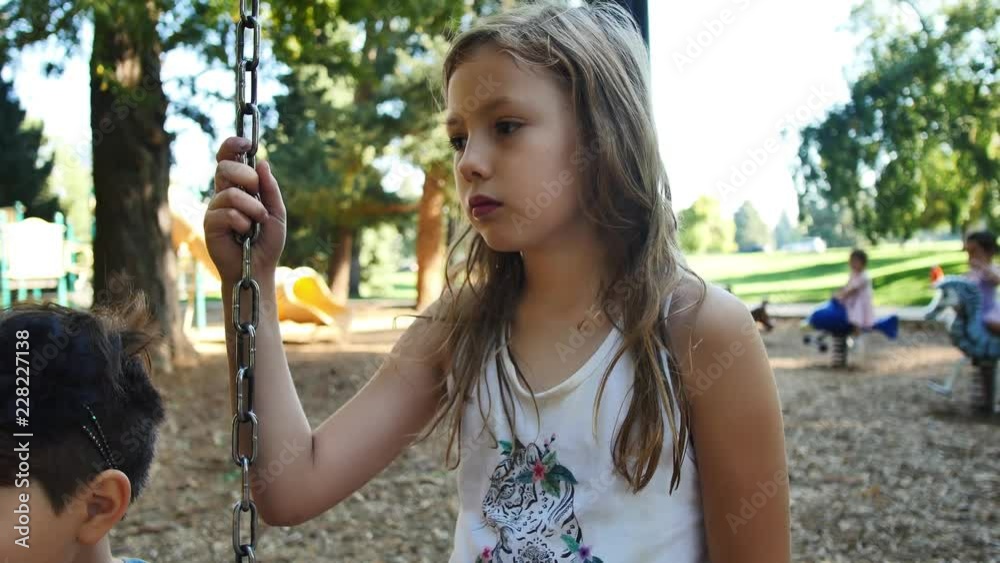 Little blonde girl stands by swings as friend is bullied