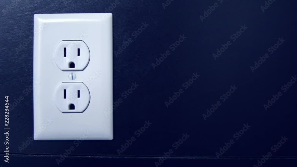 Light turns on and off at night as a cord is plugged into the bottom outlet and removed from an American electrical socket, copy space right