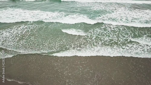 Aerial view ocean blue and green waves break on white sand beach. Sea waves on the beautiful beach aerial view drone 4k static shot. Tropical beach resort on summer holiday. High flying over Coastline