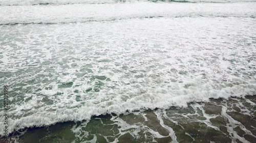Aerial view ocean blue and green waves break on white sand beach. Sea waves on the beautiful beach aerial view drone 4k static shot. Tropical beach resort on summer holiday. High flying over Coastline