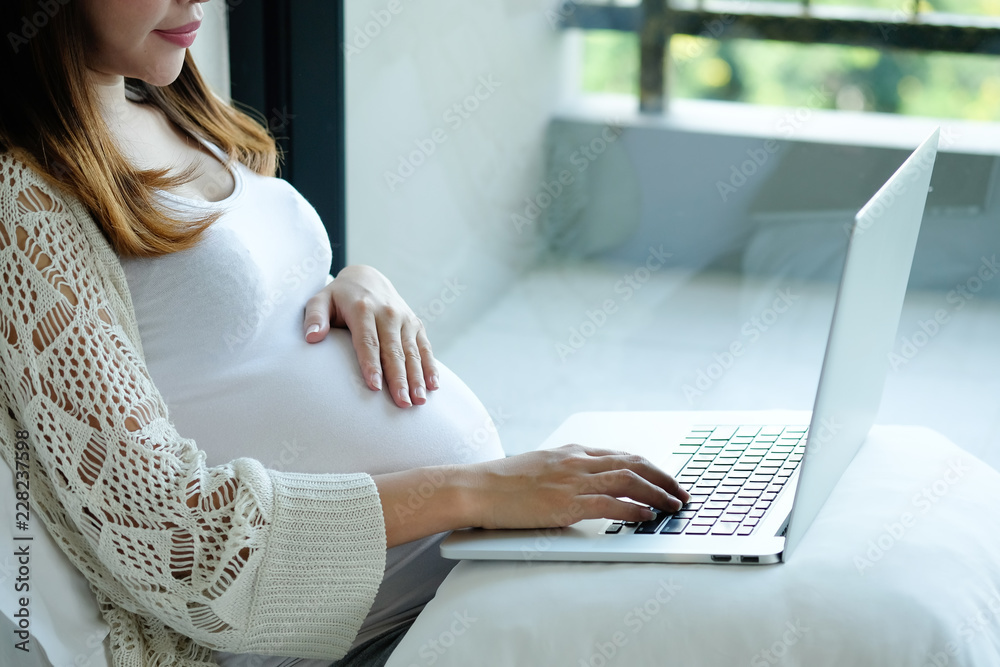 Naklejka premium Pregnant woman is using laptop computer on bed.