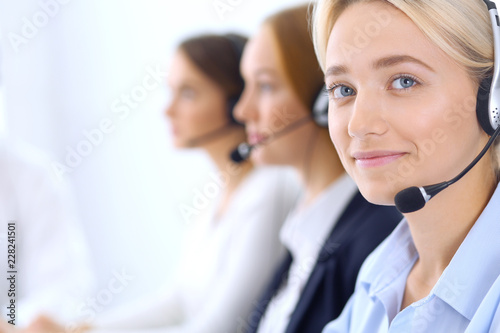 Group of call center operators at work. Focus at blonde beautiful business woman in headset