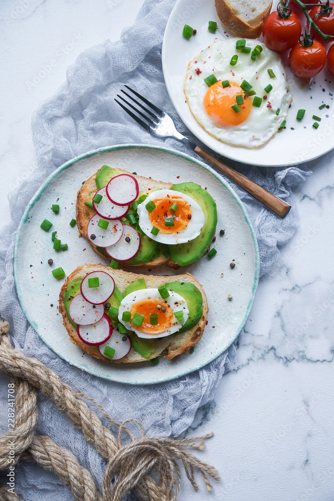 Healthy breakfast, Toasts with avocado, egg, radish, sweet onions and tomatoes, Diet food, On a light marble background, Selective focus, Top view