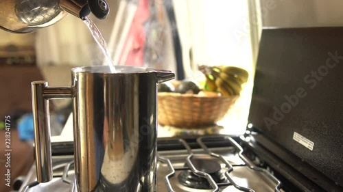Man pours boiling water from a tea pot into a stainless steel french press