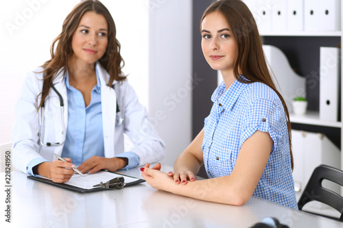 Doctor and happy patient talking while sitting at the desk. The physician or therapist discussing healthy lifestyle. Health care, medicine and patient service concept