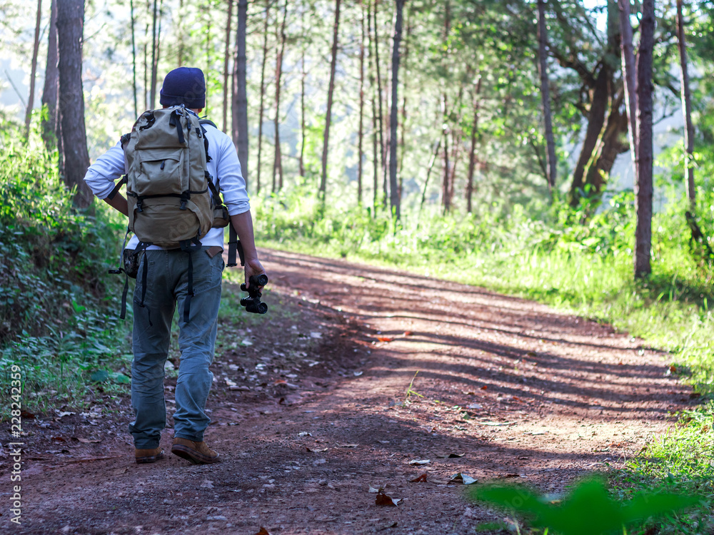 Young man with backpack and holding a binoculars walking on trail in forest