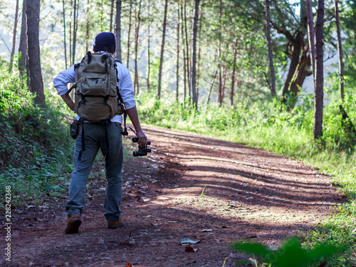 Young man with backpack and holding a binoculars walking on trail in forest