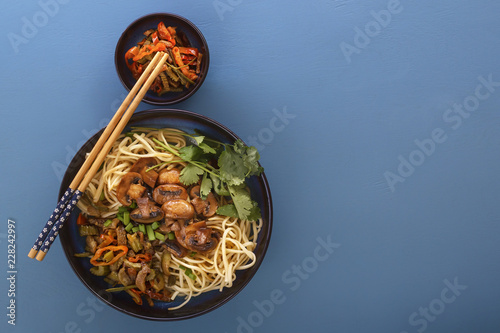 Traditional Chinese noodles noodles with fried meat and salad in a porcelain plate on a blue table. Copy space. Top view
