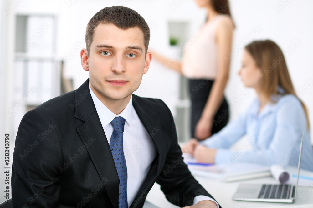 Portrait of a young business man  against a group of business people at a meeting