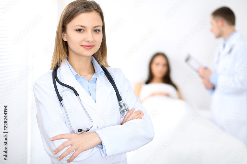 Medicine doctor standing and smiling on the background with patient in the bed Medicine doctor standing and smiling on the background with patient in the bed