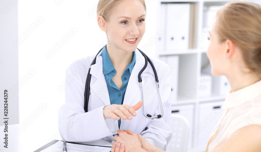 Blonde female doctor and patient talking in hospital office. Health care and client service in medicine Blonde female doctor and patient talking in hospital office. Health care and client service in medicine