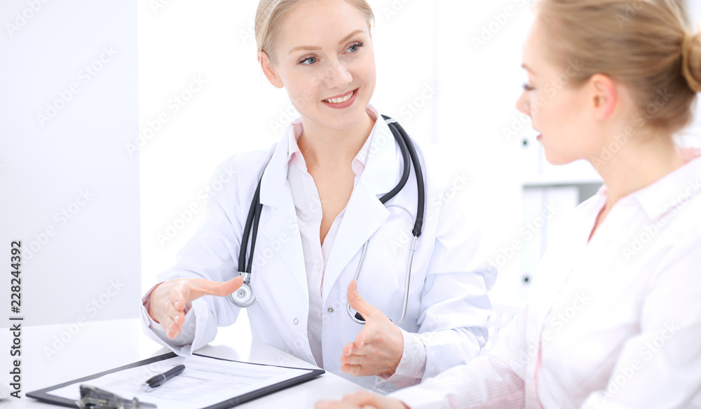 Blonde female doctor and patient talking in hospital office. Health care and client service in medicine Blonde female doctor and patient talking in hospital office. Health care and client service in medicine