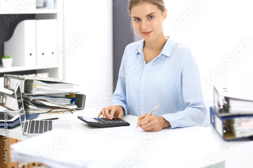 Woman bookkeeper or financial inspector calculating or checking balance, making report. Internal Revenue Service at work with financial document. Tax and audit concept