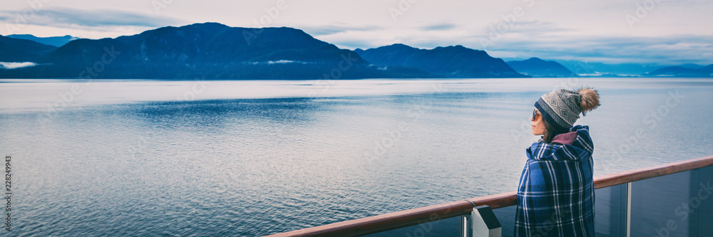 Alaska cruise travel luxury vacation woman banner panorama of inside passage scenic landscape background on balcony deck enjoying view of mountain range. Asian girl tourist with wool blanket.