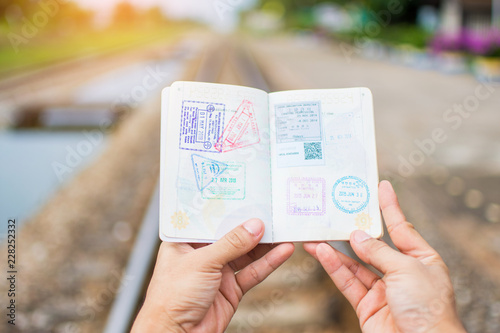 Hand holding passport show immigration stamps on passport with railway background. subject is blurred. photo