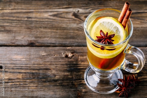 Hot spiced Apple cider Toddy with lemon, honey and cinnamon stick in glass on wooden background