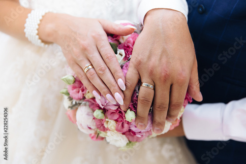 Close-up of the hands of the newlyweds with wedding rings  gently touch the wedding bouquet of peonies.