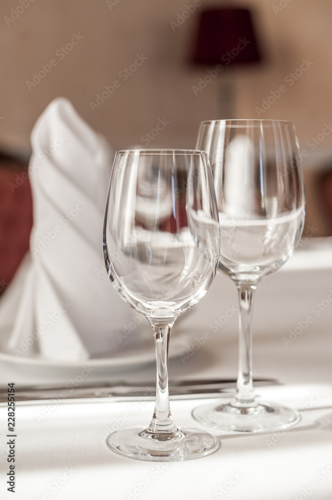 Two empty wine glasses on a served table. White tablecloth, glasses, plates, appliances, red furniture Two empty wine glasses on a served table. White tablecloth, glasses, plates, appliances, red furniture