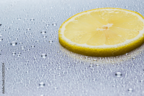 Slice of lemon on a steel reflective background with water drops close-up