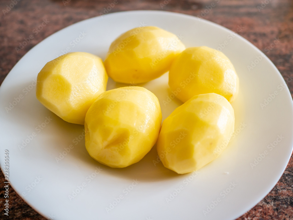Top view of peeled raw potatoes on white plate in kitchen