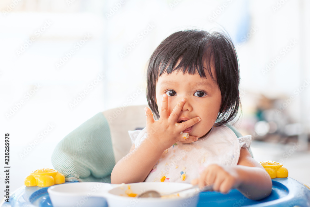 Cute baby asian child girl eating healthy food by herself and making a mess on her face and hand Cute baby asian child girl eating healthy food by herself and making a mess on her face and hand